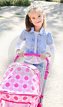 Cute smiling little girl playing with her toy carriage