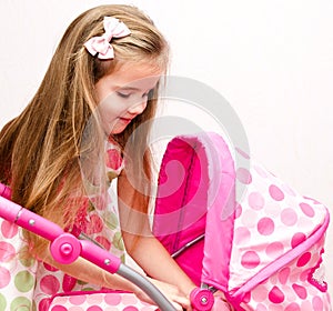 Cute smiling little girl playing with her toy carriage and doll