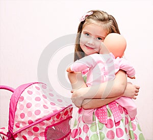 Cute smiling little girl playing with her toy carriage and doll