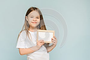 Cute smiling little girl pointing to an empty space in a frame on a blue background. Copy space. Place for advertising