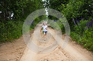 A cute smiling little girl running barefoot in a countryside landscape along a country path