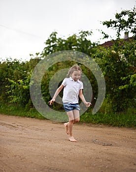 A cute smiling little girl running barefoot in a countryside landscape along a country path