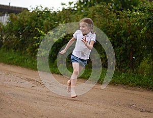 A cute smiling little girl running barefoot in a countryside landscape along a country path