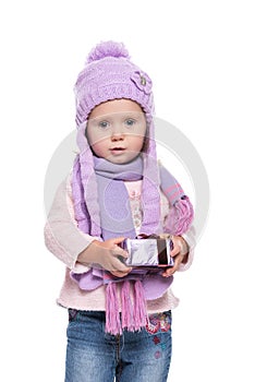 Cute smiling little girl wearing violet knitted scarf and hat, holding christmas gift isolated on white background. Winter clothes