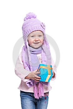 Cute smiling little girl wearing violet knitted scarf and hat, holding christmas gift isolated on white background. Winter clothes