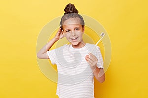 Cute smiling little girl with wet hair wearing casual white T-shirt standing isolated over yellow background taking care of her