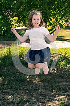 Cute smiling little girl in white t-shirt and dark blue skirt jump outdor in field in sunset