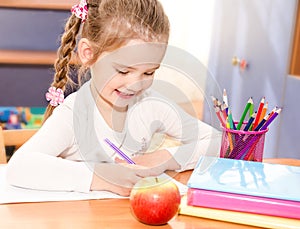 Cute smiling little girl is writing at the desk