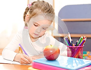 Cute smiling little girl is writing at the desk