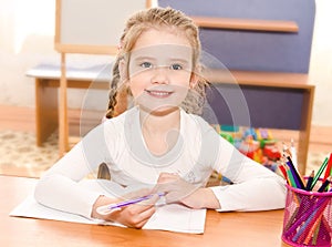 Cute smiling little girl is writing at the desk