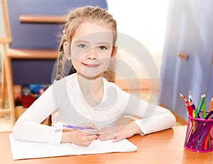 Cute smiling little girl is writing at the desk