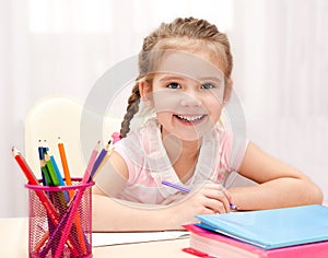 Cute smiling little girl is writing at the desk