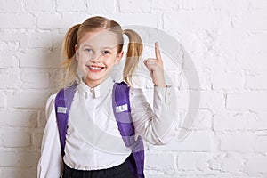 Cute smiling schoolgirl in uniform standing on light background and showing thumb up.