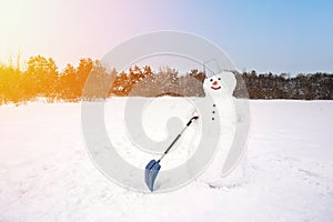 Cute smiling snowman with a shovel in a field covered with snow. The concept of snow removal.