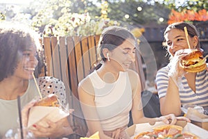 Cute smiling teenage girls are sitting in open air cafe and eating fast food