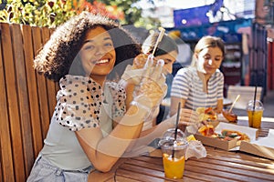 Cute smiling teenage girls are sitting in open air cafe and eating fast food