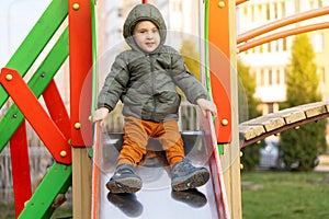 A cute smiling toddler boy of three years rides on a swing in a playground.