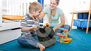 Cute smiling toddler boy tidying up his room and picking toys in bag