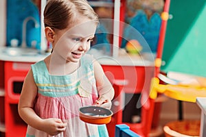 Cute smiling toddler girl playing with toy kitchen at home