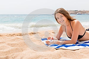 Cute and smiling woman is applying sunscreen on her hand with the finger sunbathing on the towel at the beach