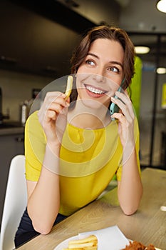 Cute smiling woman holding french fries talking with smartphone