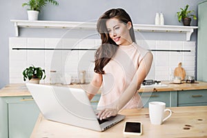 Cute smiling woman using laptop computer in her room. Online shopping concept