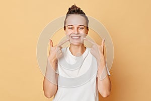 Cute smiling woman wearing white T-shirt washes hair standing with hair balm on her head isolated over beige background pointing