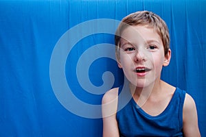 Cute smiling young boy with blue eyes on the blue background. Astonishment emotions design with copy space