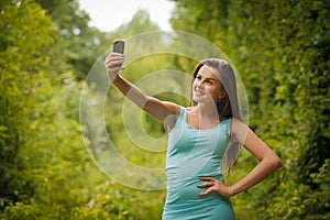 Cute smiling young Caucasian teenage girl taking a selfie outdoors on sunny summer day