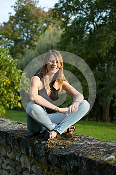 Cute Smiling Young Woman Sitting in the Park During Sunset in Jeans and Black Shirt and Looking at the Camera.