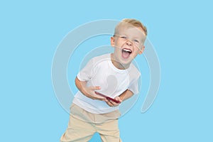 Cute smilling child boy with smartphone on blue background. Advertising of educational applications on a mobile phone