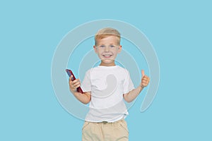 Cute smilling child boy with smartphone on blue background. Advertising of educational applications on a mobile phone