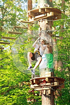 Cute, sporty young boy in helmet and white t shirt in the rope adventure park in the summer. Active sport life