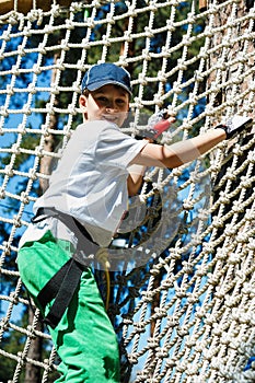 Cute, sporty young boy in helmet and white t shirt in the rope adventure park in the summer. Active sport life