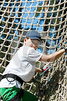 Cute, sporty young boy in helmet and white t shirt in the rope adventure park in the summer. Active sport life