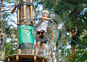 Cute, sporty, young boy in white helmet spends his free time in the rope adventure park on a sunny day. Active lifestyle