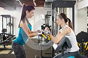 Cute sporty young woman doing exercise in a fitness center with her personal coach