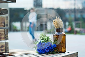 Cute still life of a bouquet of cornflowers and a glass jar with dried ears on the background of an urban landscape