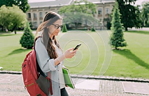 Cute student girl walking and loock at mobile phone with a university building in the background