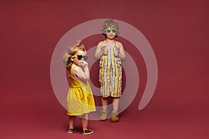 Cute stylish children in fashionable clothes posing on pink background. A little girl in a dress and sunglasses and a