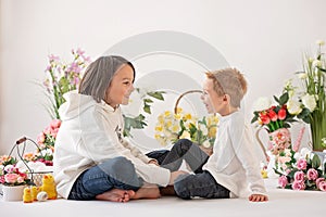 Cute stylish toddler child and older brother, boys with white shirt, playing with eggs and chocolate bunny on Easter decoration