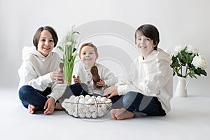 Cute stylish toddler child and older brother, boys with white shirt, playing with eggs and chocolate bunny on Easter decoration