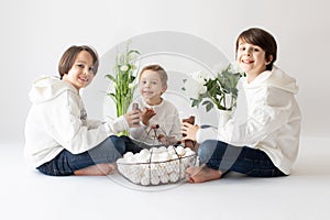 Cute stylish toddler child and older brother, boys with white shirt, playing with eggs and chocolate bunny on Easter decoration