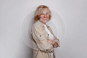 Cute successful mature woman with short blonde bob hair standing with arm crossed against white background, portrait.