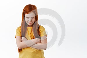 Cute sulking little girl with ginger hair and freckles cross arms on chest, upset about unfair thing, pouting and acting