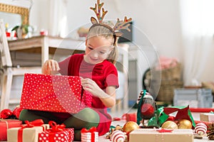 Cute super excited young girl opening large red christmas present while sitting on living room floor. Candid family christmas time