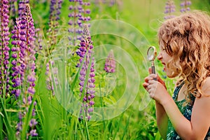 Cute surprised child girl exploring nature with loupe on summer field