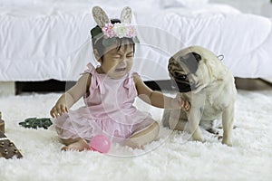 Cute Sweet Adorable Asian Baby wearing pink dress Sitting on white carpet Crying with dog pug breed