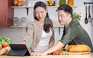 Cute sweet Asian boyfriend girlfriend couple cooking breakfast together in kitchen, looking tablet, watching for method and recipe