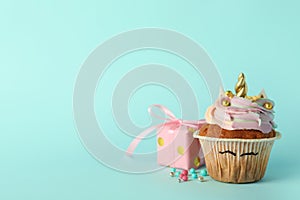 Cute sweet unicorn cupcake and gift box on light turquoise background, space for text